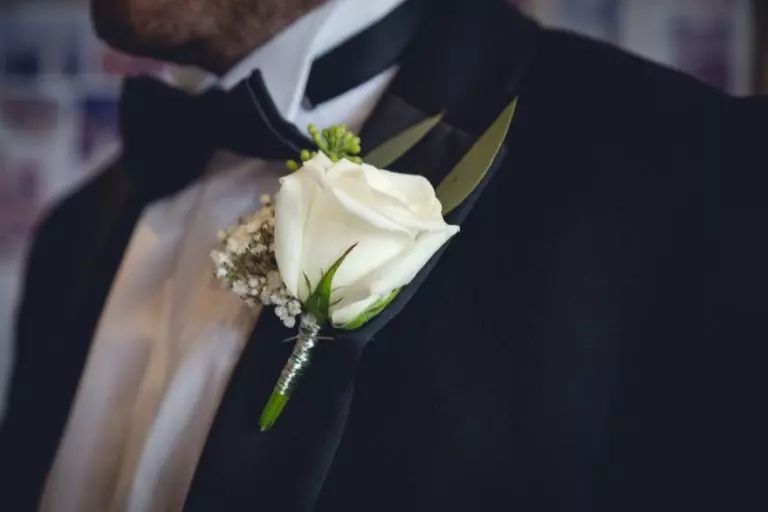 Gros plan photo sur la boutonnière du marié : une rose blanche sur le revers de sa veste
